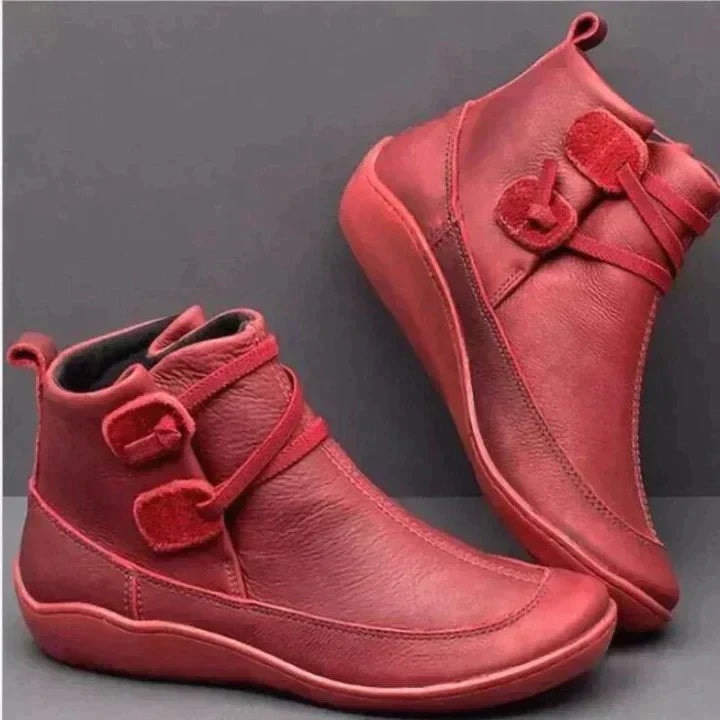 Red ankle boots displayed in opposite orientations, highlighting the wraparound straps, buckle details, rounded toes, and low-profile soles.