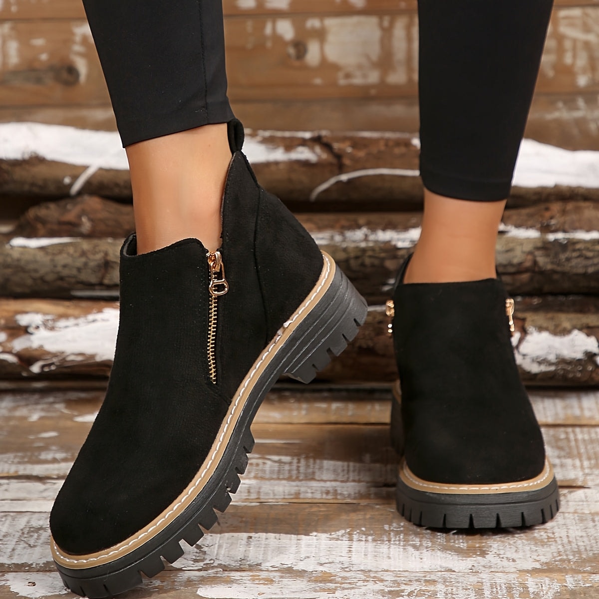 Black ankle boots worn on wooden steps, showing the front shape, side zips, and rugged soles.