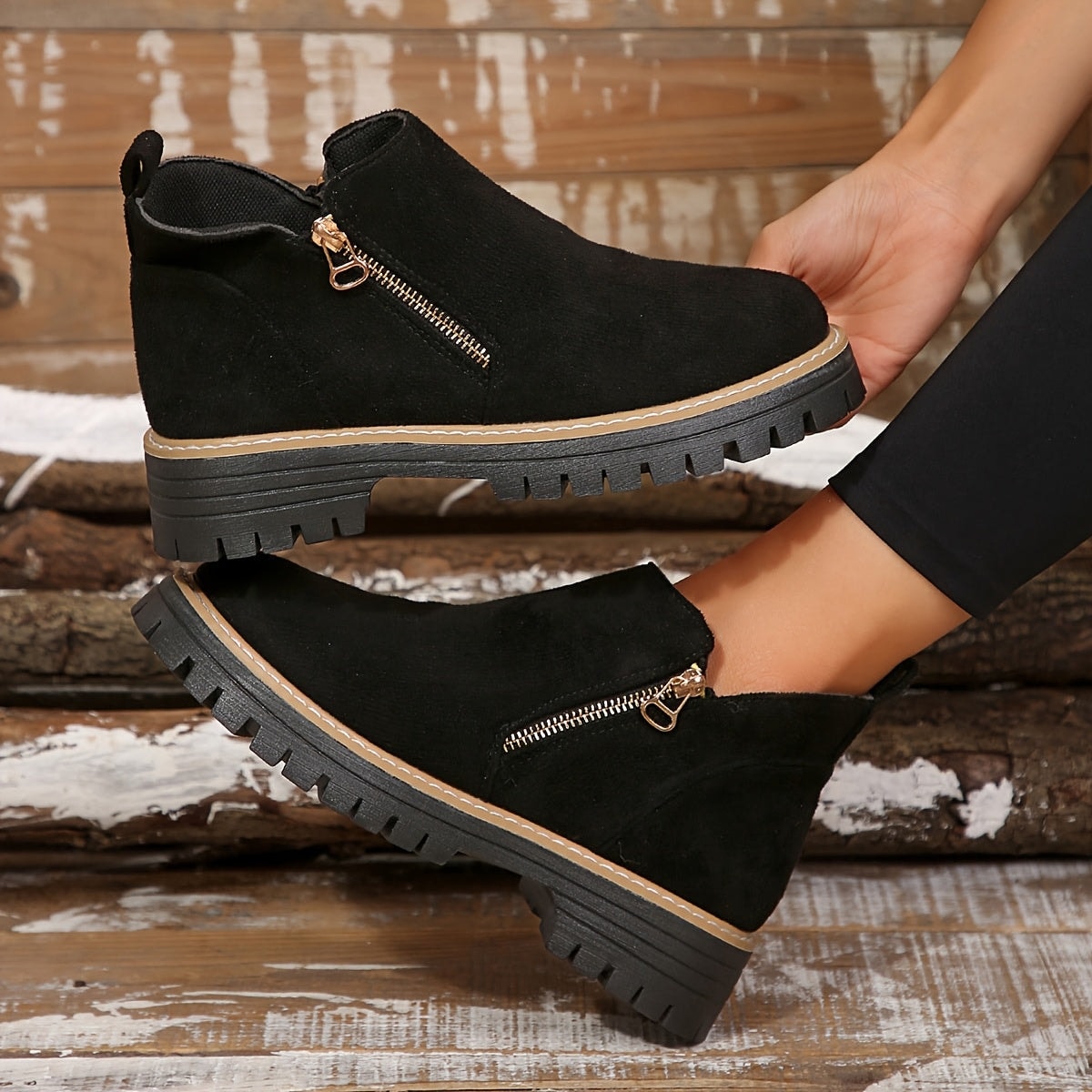 Black ankle boots lifted in a side profile to emphasize the zip closures, contrast stitching, and lugged soles.