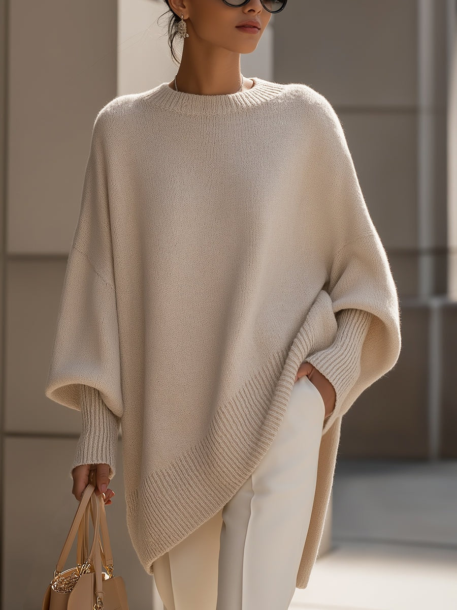 Cream asymmetric poncho sweater with a crew neckline, wide batwing sleeves, ribbed trim, and longline hem styled with light trousers.