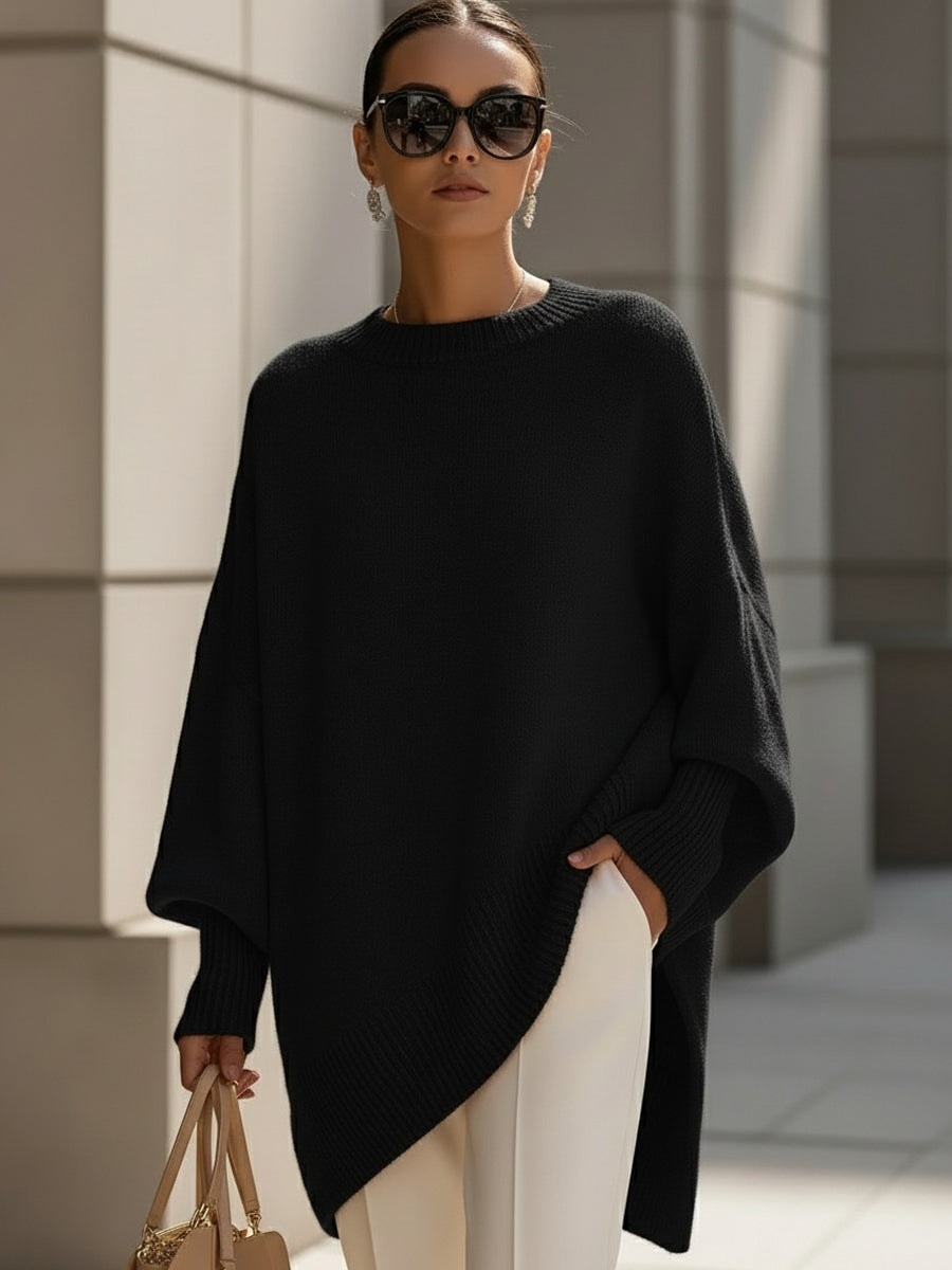 Black longline poncho sweater with a clean crew neckline, wide sleeves, ribbed trim, and an asymmetric pointed hem.