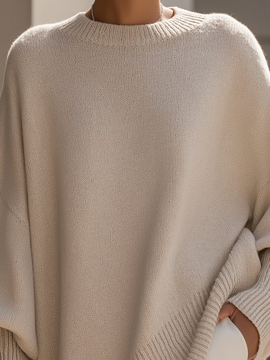 Close view of the cream poncho sweater showing its ribbed crew neckline and relaxed batwing shape.
