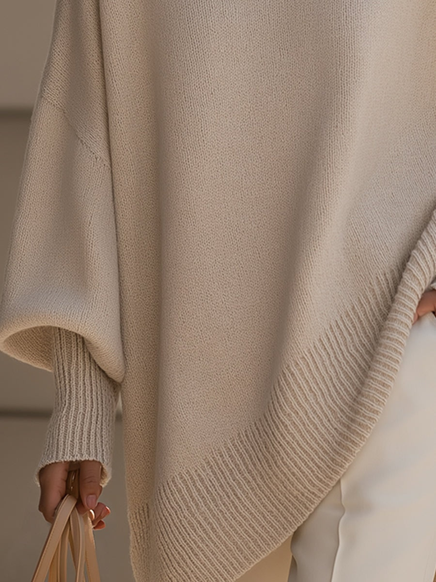 Detail of the cream sweater’s sweeping asymmetric hem and wide ribbed trim beside light trousers.