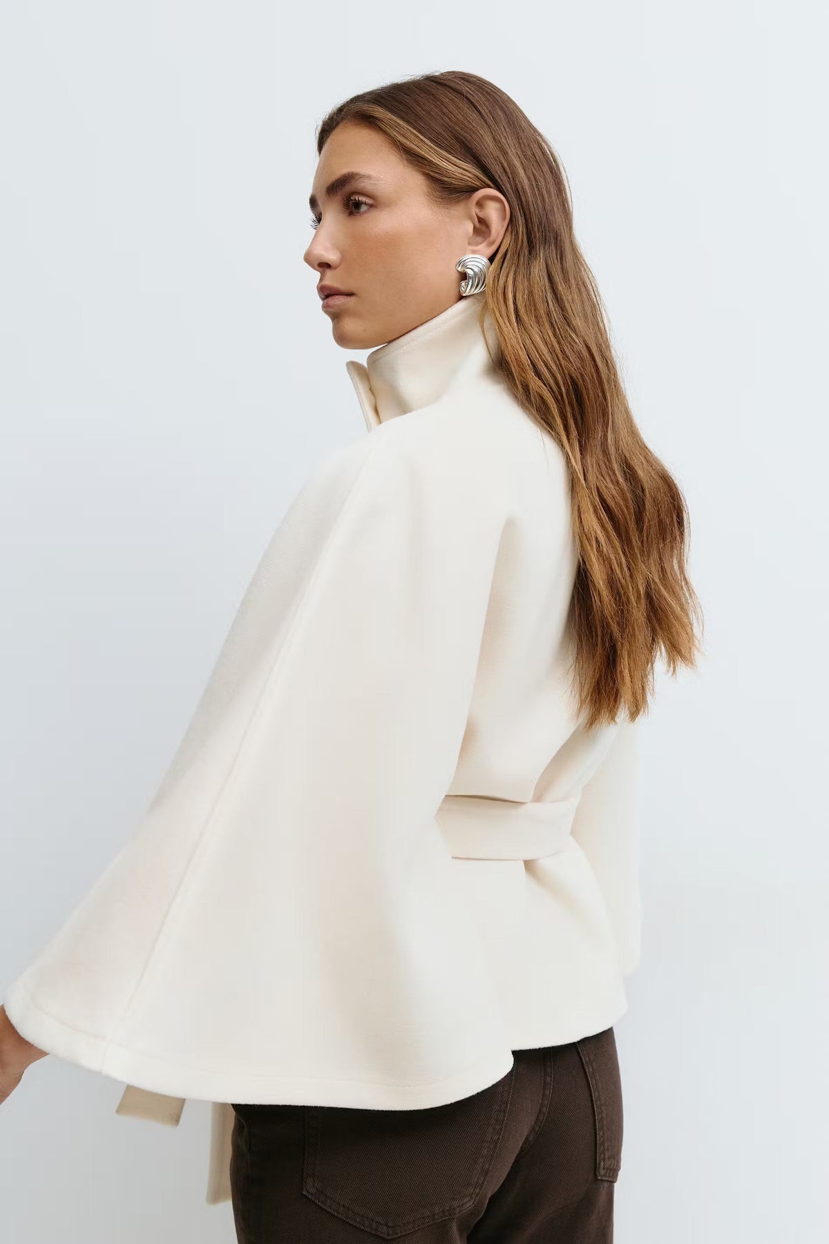 Side-back view of the cream cape jacket, highlighting the flowing wide sleeve and waist tie.