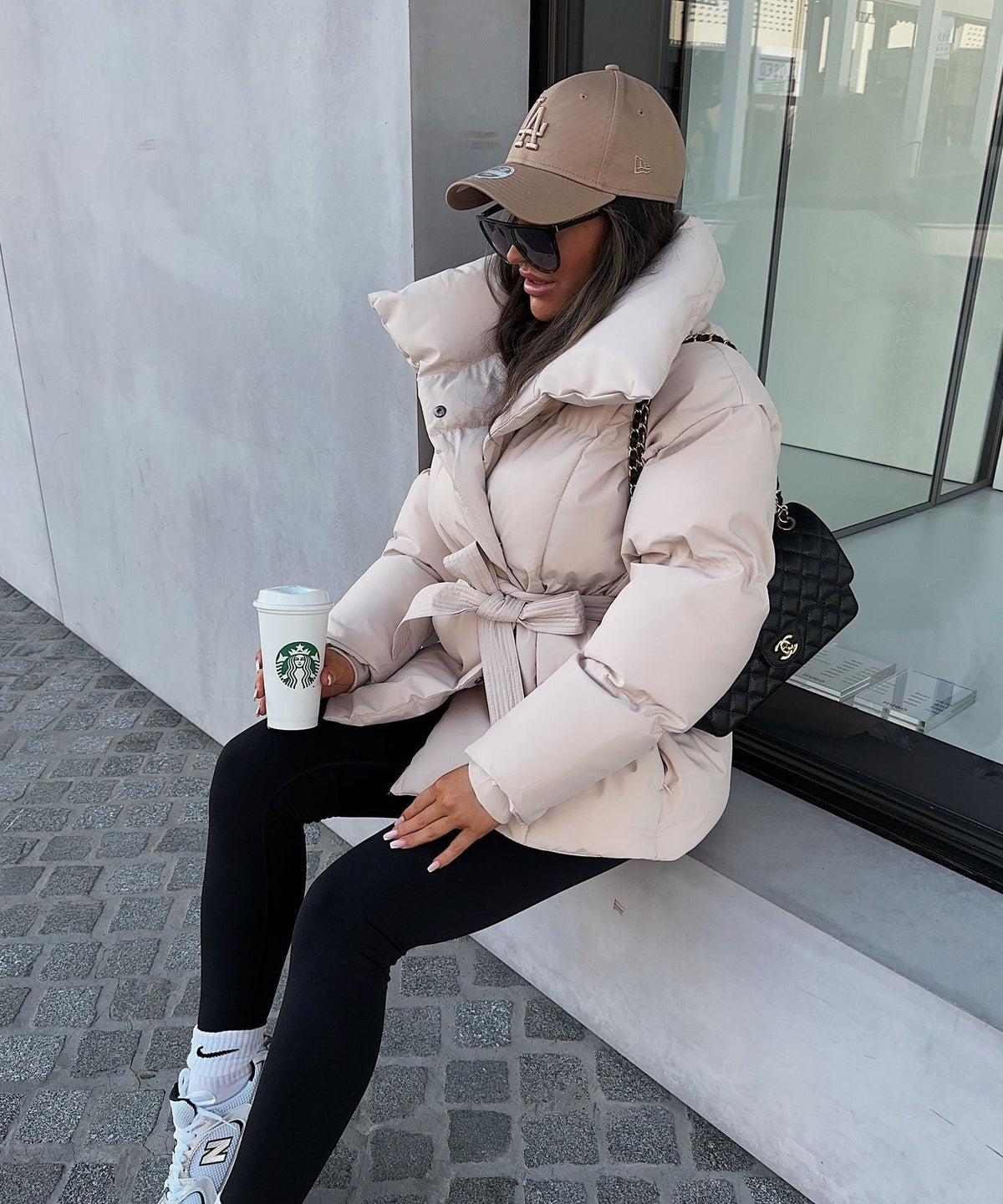 Side view of the light beige puffer jacket showing its padded sleeves, raised collar, tied waist, and short length.