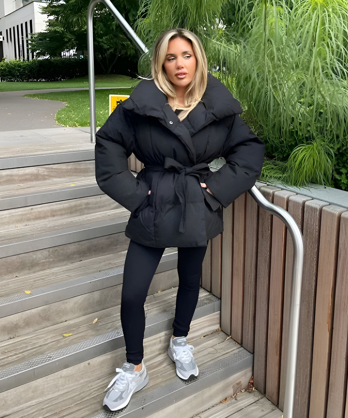 Full-body view of the black puffer jacket cinched at the waist with its tie, styled with leggings and sneakers.
