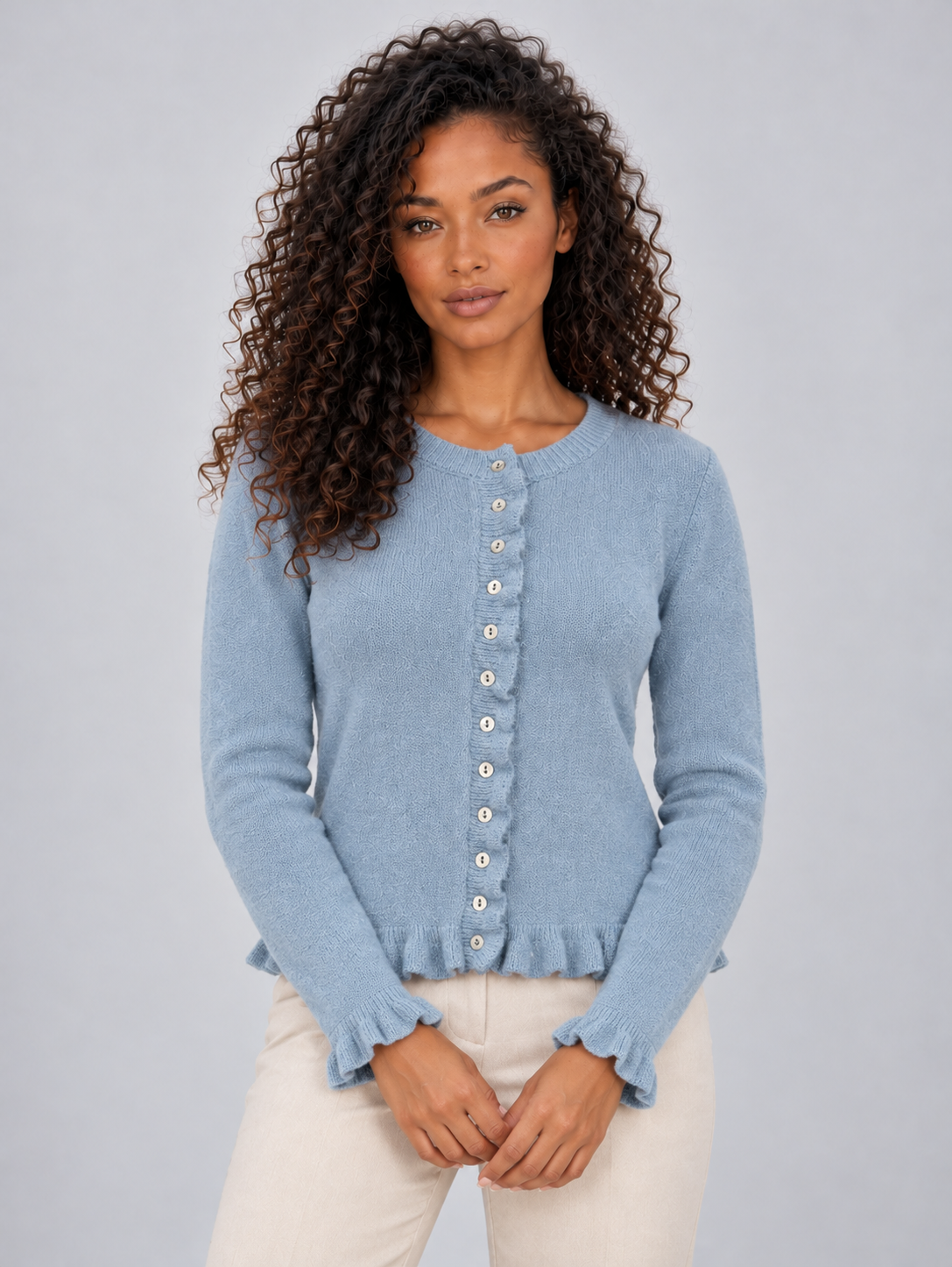 Blue cardigan styled closed, featuring a row of front buttons, long sleeves, and delicate ruffles at the hem and cuffs.