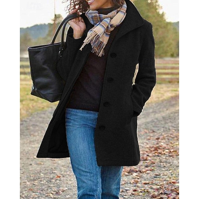 Black mid-length coat with a notched collar and button front styled with jeans in an outdoor setting.