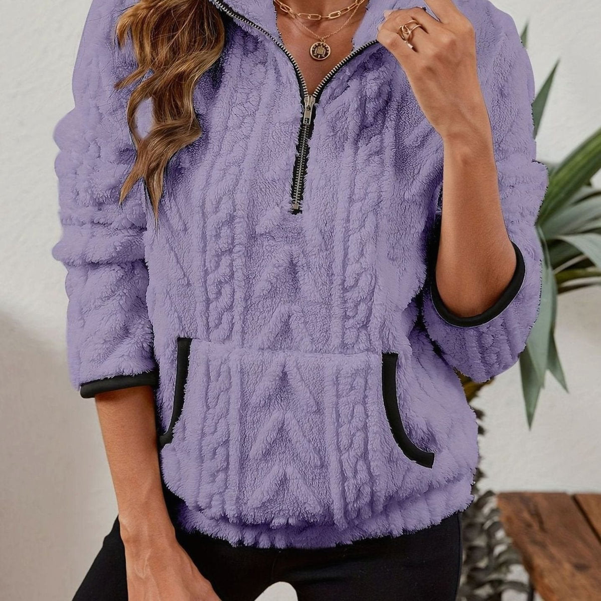Close front view of the pullover in lavender, showing the raised cable design, loose sleeves, and dark-trimmed hand pocket.