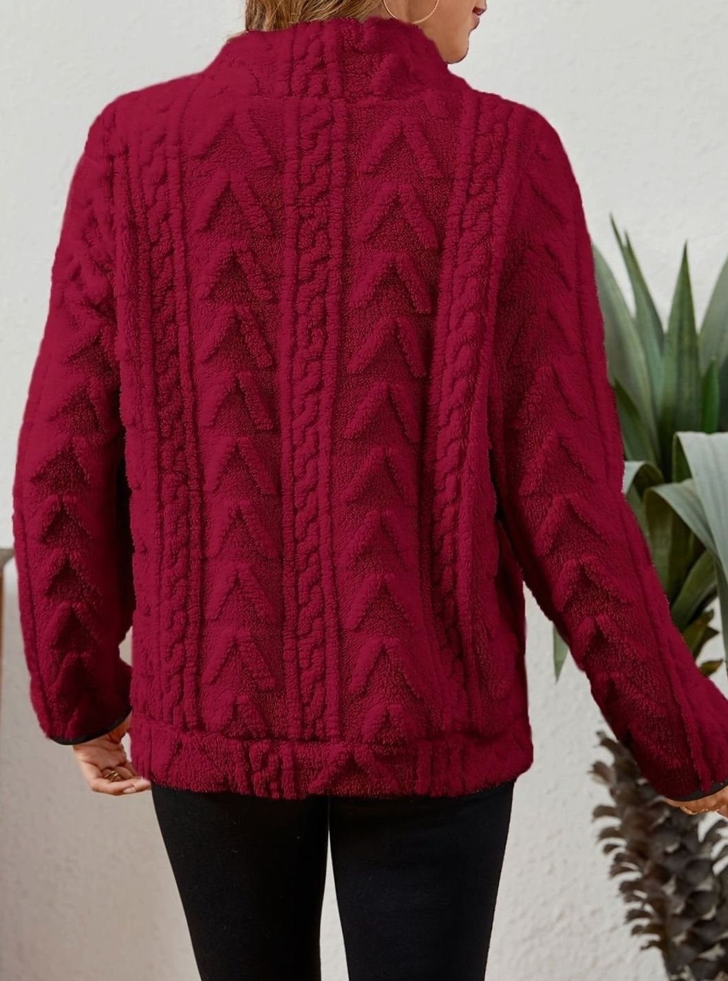 Back view of the burgundy pullover showing its raised cable-textured pattern, loose shape, long sleeves, and ribbed hem.