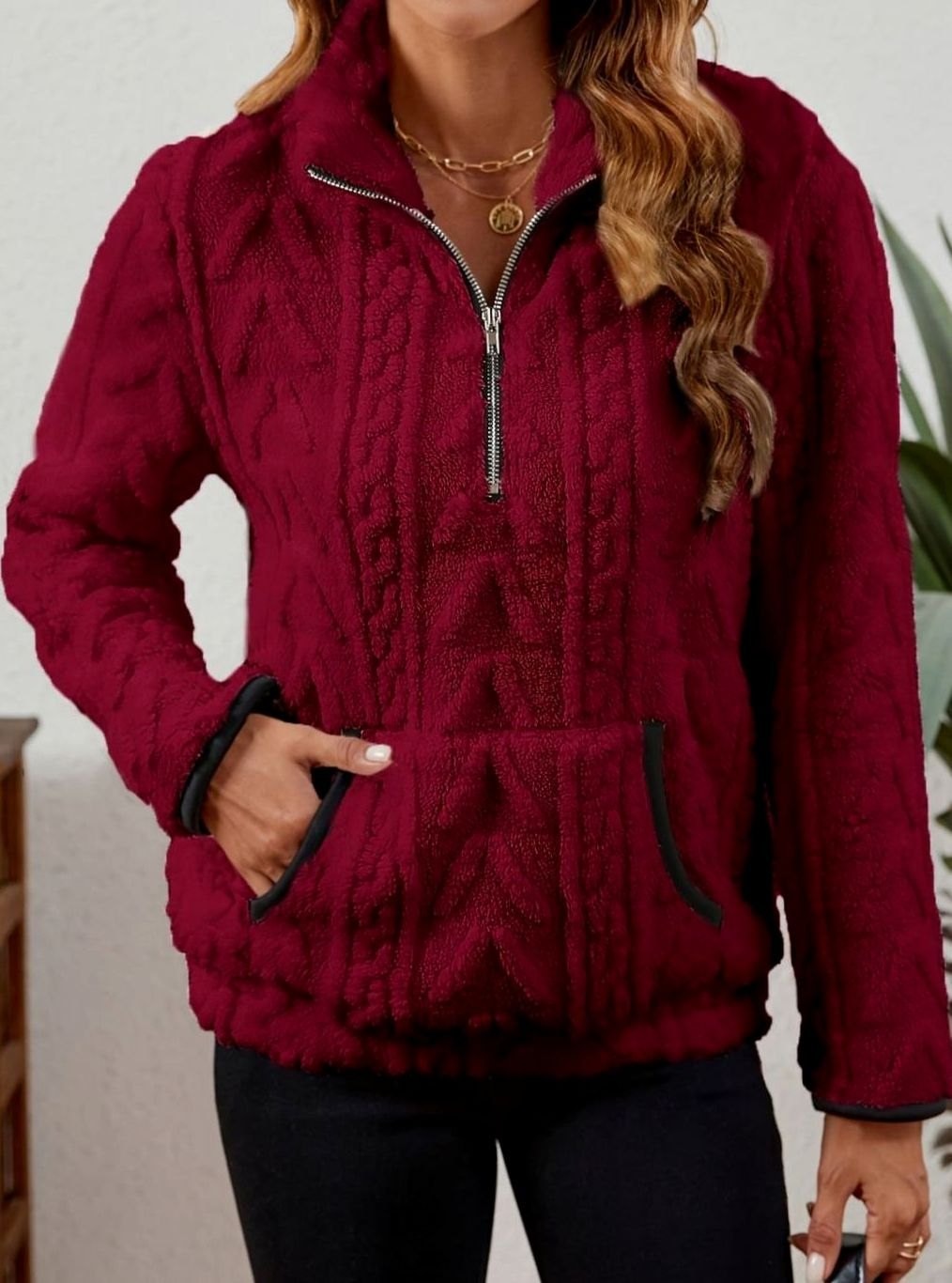 Front view of the burgundy pullover with one hand in the kangaroo pocket, highlighting the textured body and contrasting pocket trim.