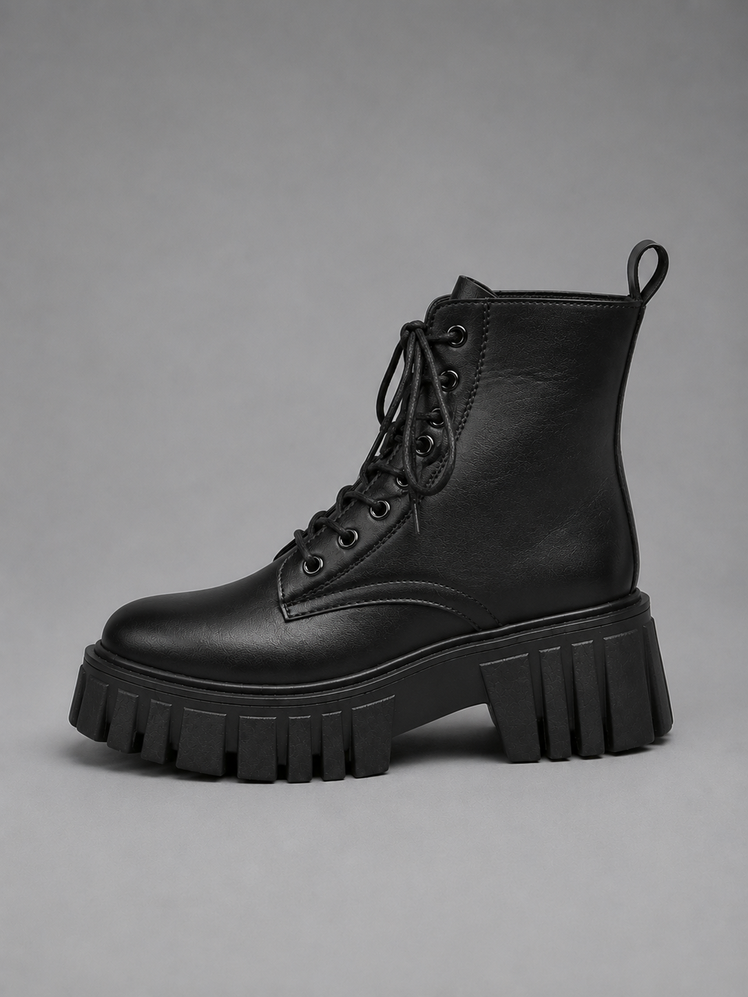 Black platform combat boot shown in side profile, highlighting the rounded toe, adjustable laces, ankle height, and rugged segmented outsole.