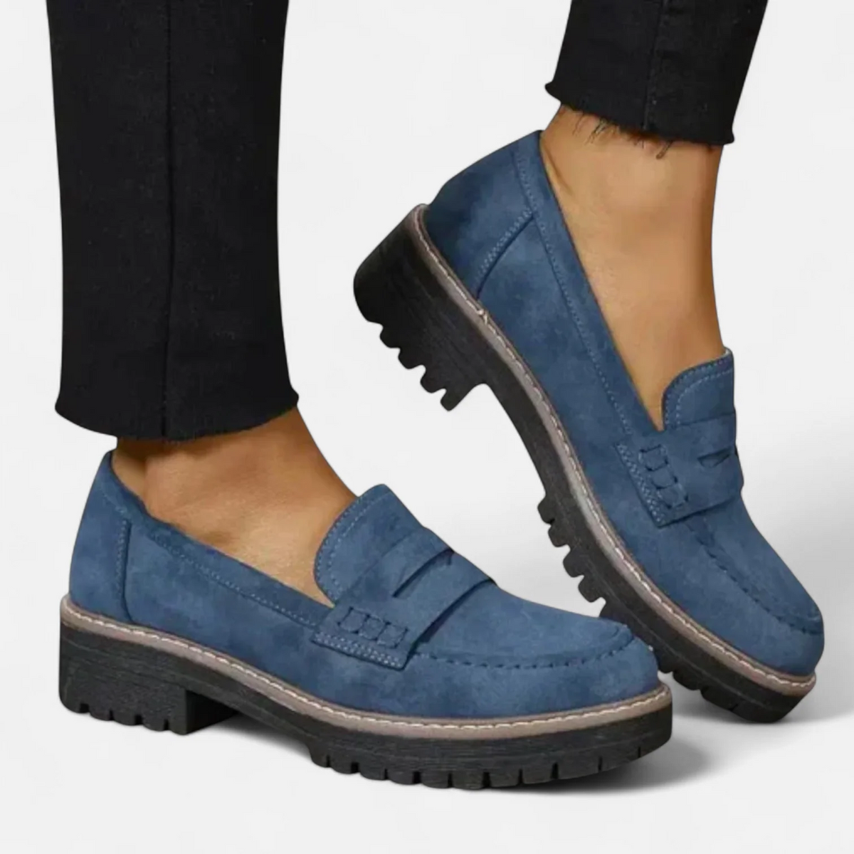 Blue chunky-sole penny loafers shown on feet with one shoe lifted to reveal the lugged outsole and low block heel.