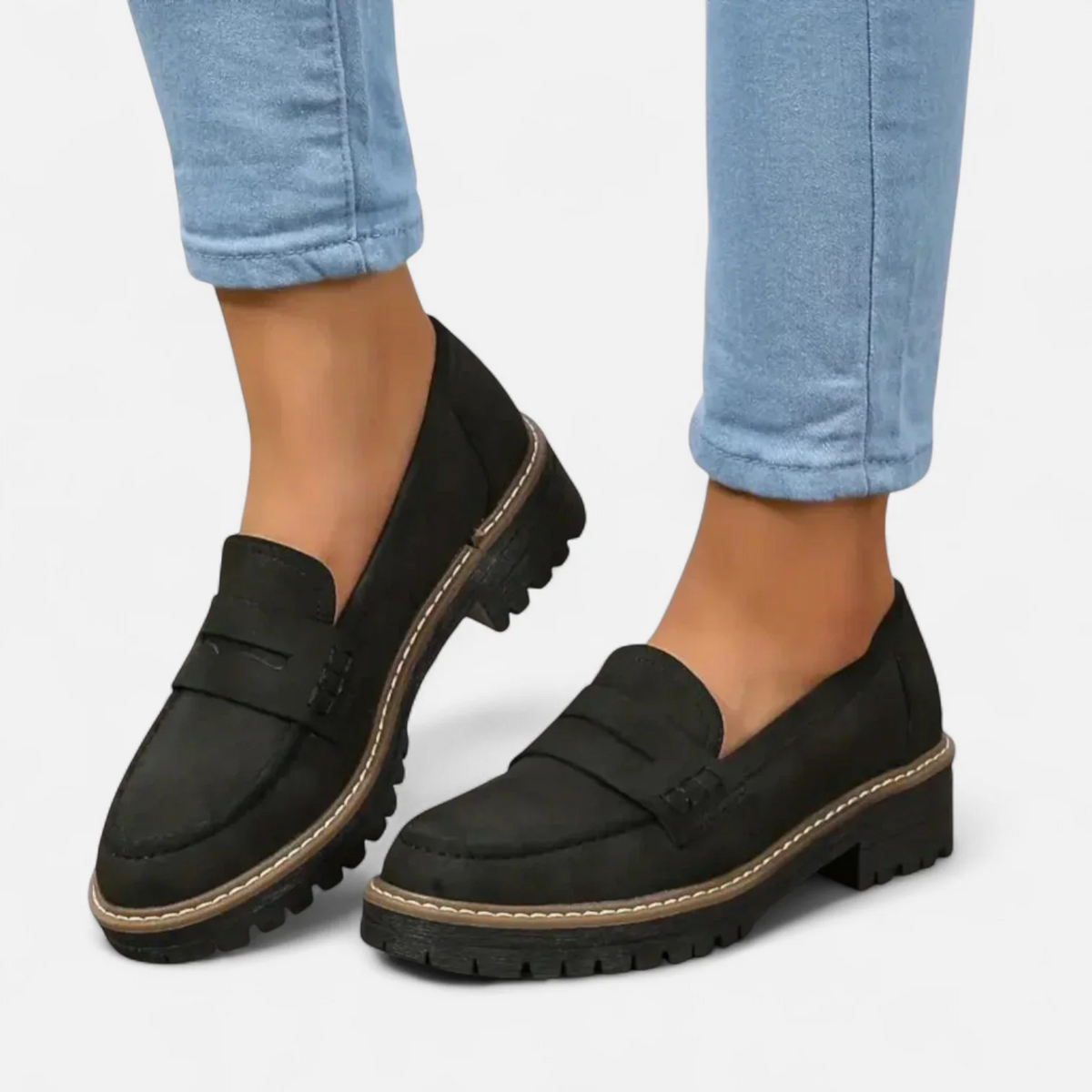 Black penny loafers worn with rolled light blue jeans in a side-by-side view, showing the low heel and chunky lug sole.