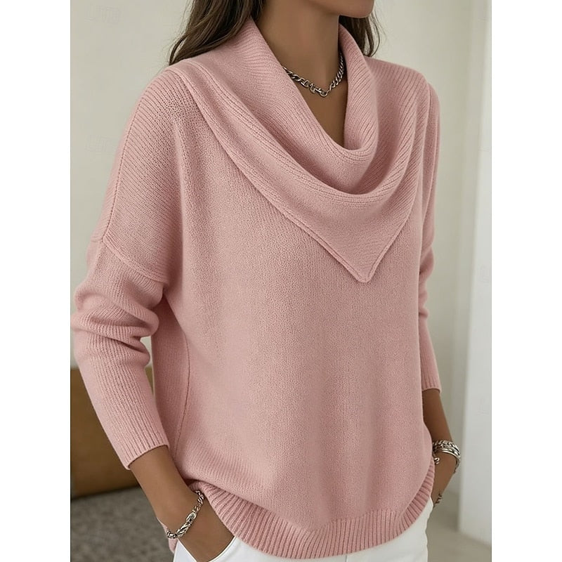 Angled front view of the pink sweater showing the relaxed silhouette, cowl neckline, and ribbed hem above white trousers.