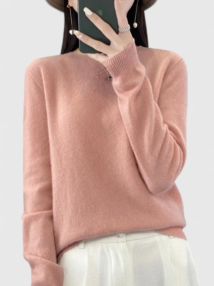 Blush pink crew neck sweater against a plain background, paired with light trousers and finished with ribbed cuffs.
