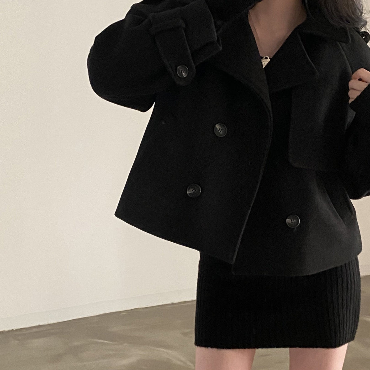 Closer view of the black cropped peacoat showing its wide collar, short hem, double-breasted button closure, and buttoned sleeve tabs.