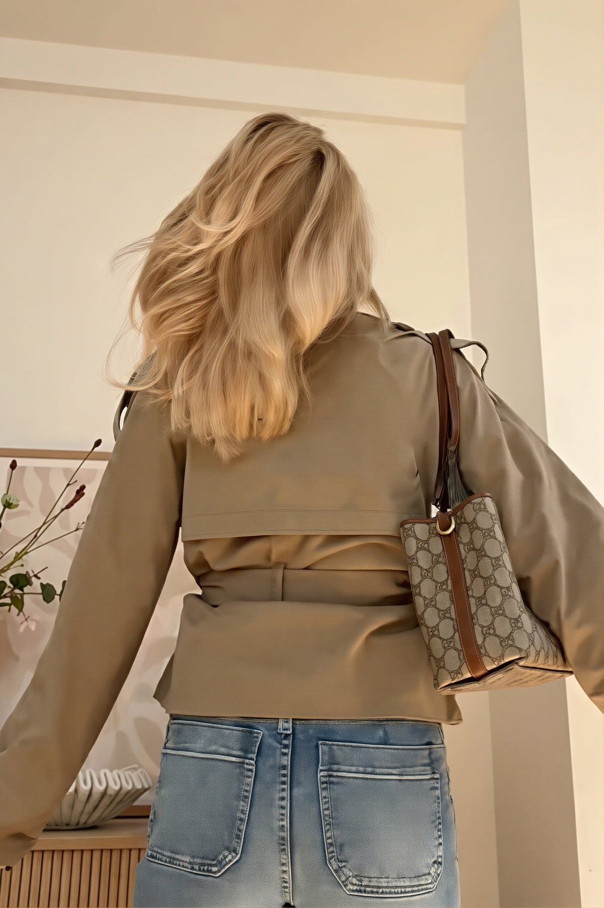 Back view of the cropped trench jacket showing its short hem, back yoke, long sleeves, and tied waist belt over jeans.