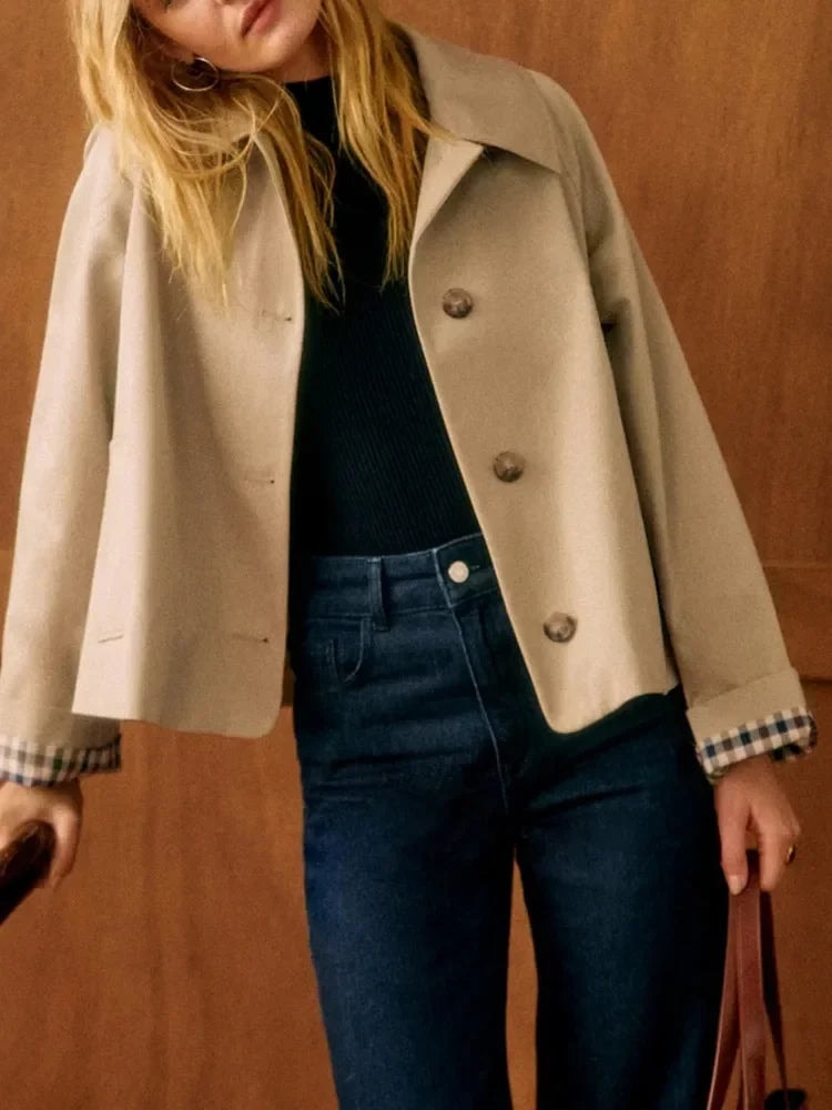 Cropped beige jacket with pointed collar, button front, and turned check cuffs styled with dark jeans.
