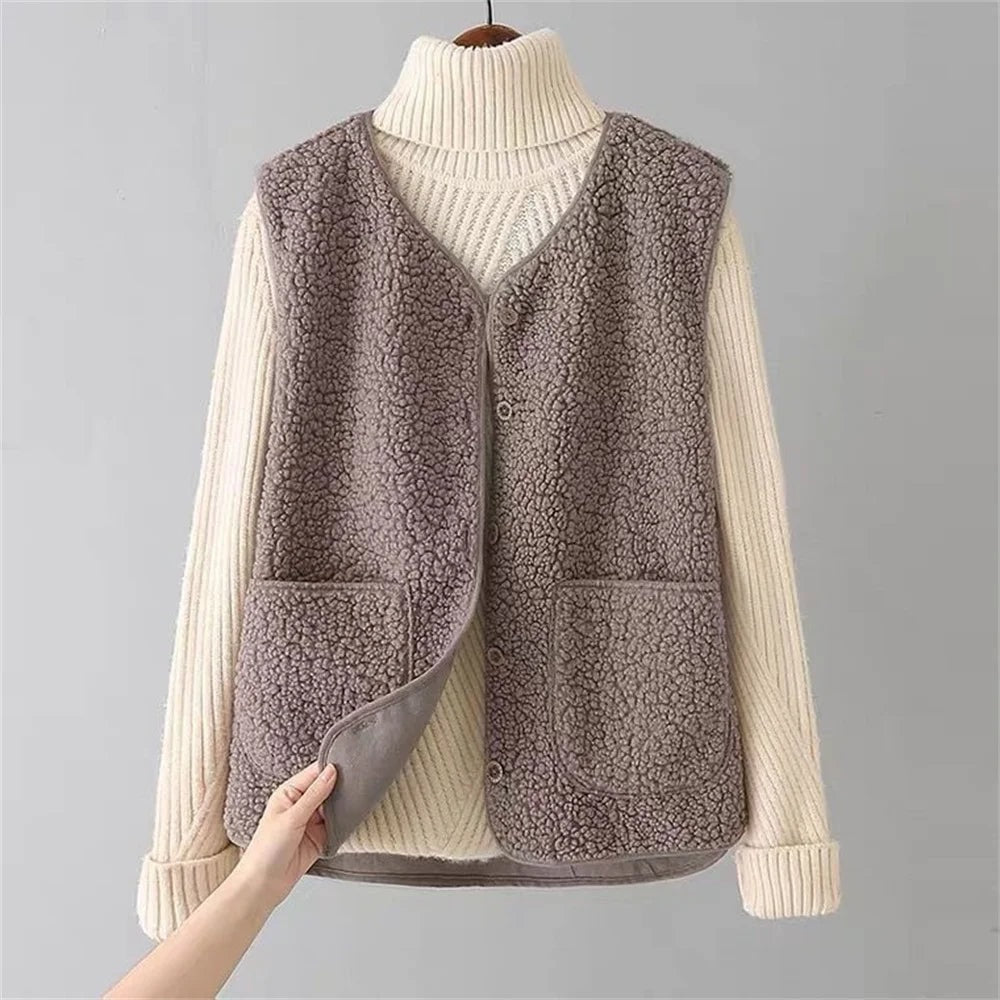 Taupe fleece vest layered over a cream sweater, with the lower front edge lifted to reveal the inside and the front buttons.