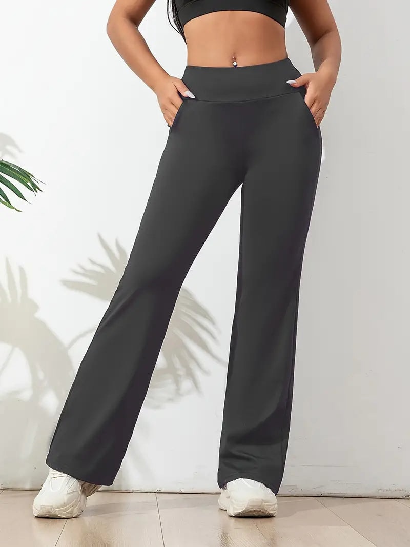 Dark gray high-waisted flared activewear pants modeled indoors with hands in the side pockets.