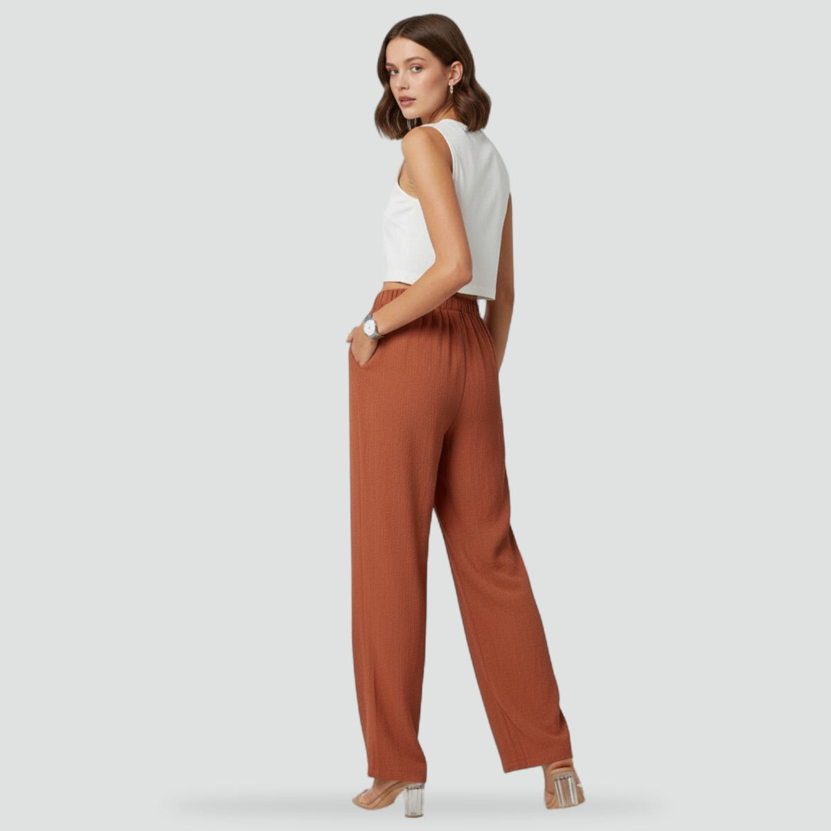 Back three-quarter view of rust high-waisted trousers, showing the elasticated back waistband and straight legs.