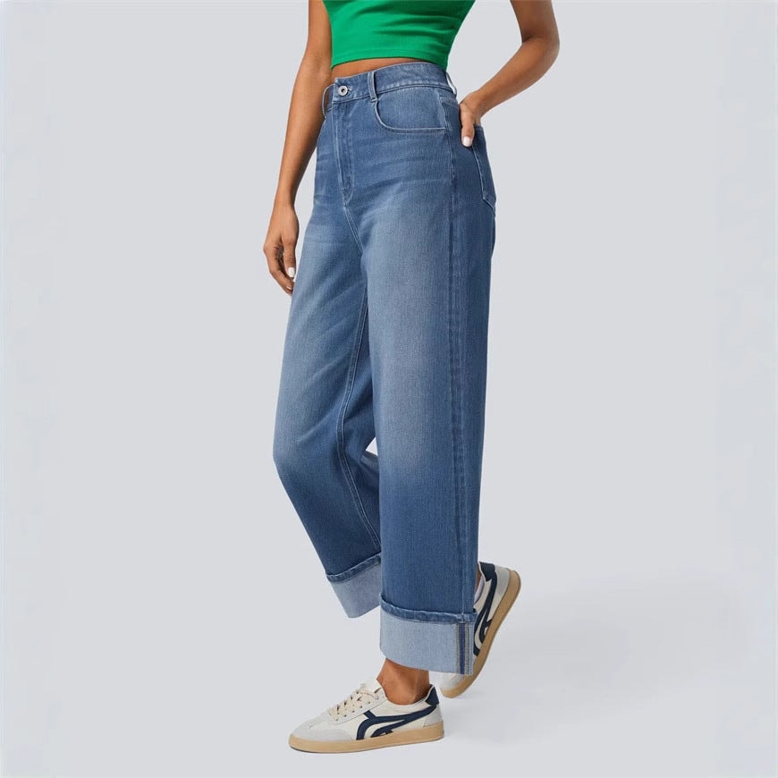 Side view showing the jeans’ high rise, flowing wide-leg cut, cropped length, and folded cuff above the sneaker.