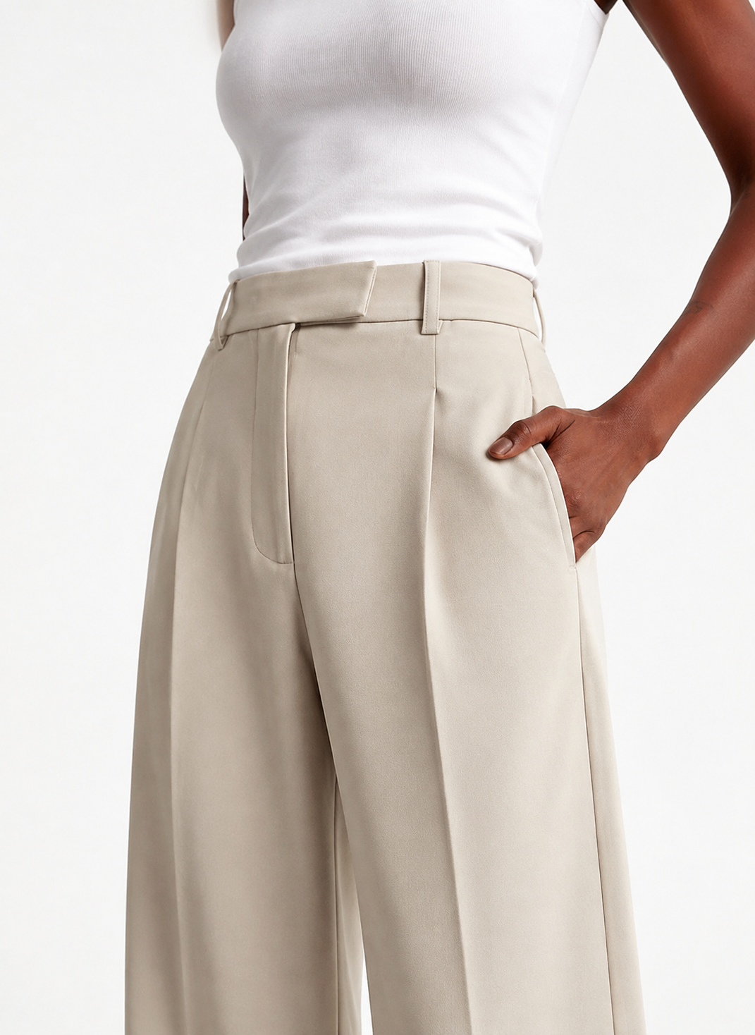 Close angled view of beige tailored trousers highlighting the waistband, pleated front, belt loops, and pocket opening.
