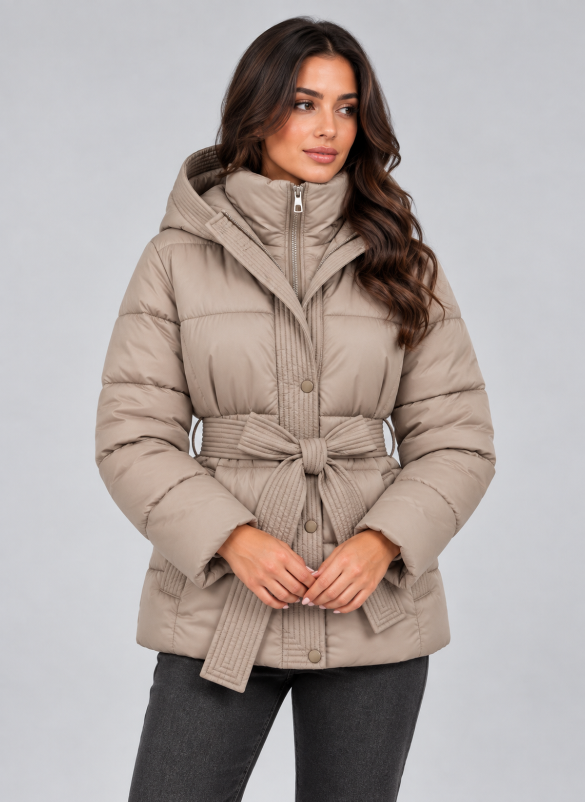 Front view of the beige quilted puffer jacket with its high collar, tied belt, long sleeves, and hands resting near the front closure.
