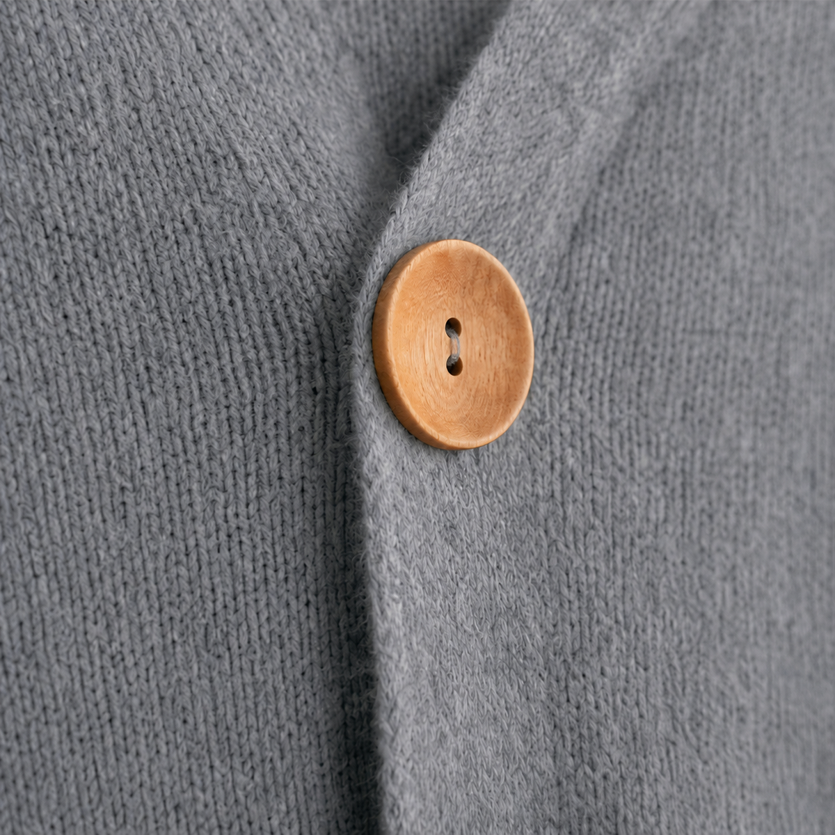 Detailed view of a round wooden button fastening the gray cardigan.
