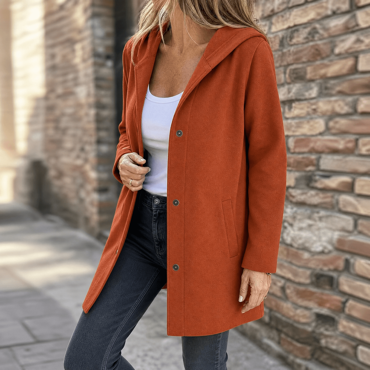 Rust-colored hooded cardigan worn partly fastened, showing its longline cut and front patch pocket.
