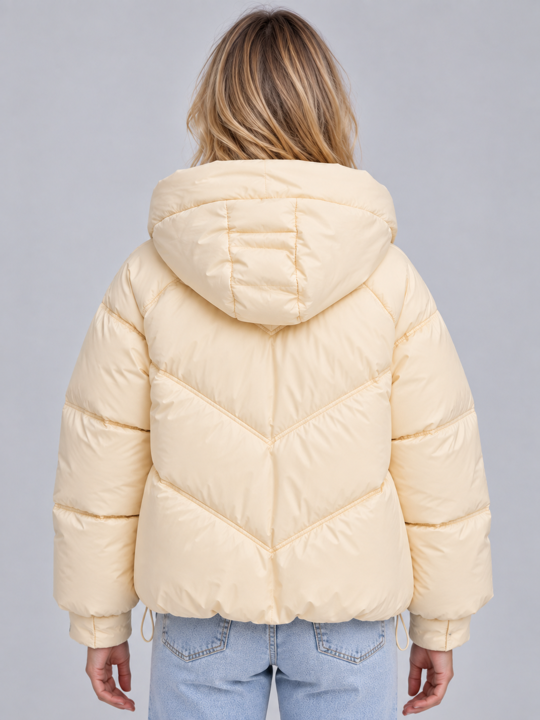Back view of the cream puffer jacket showing its attached hood and chevron-style geometric quilting across the padded silhouette.