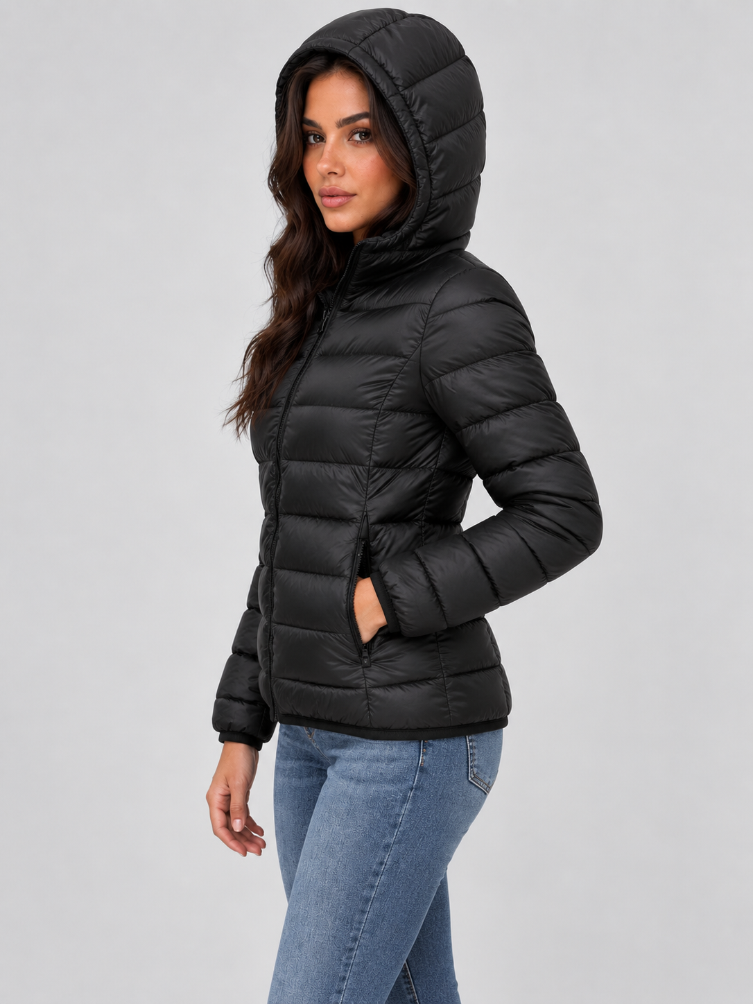 Side view of the black puffer jacket with its hood raised, full front zip, horizontal quilting, and hand placed in a side pocket.