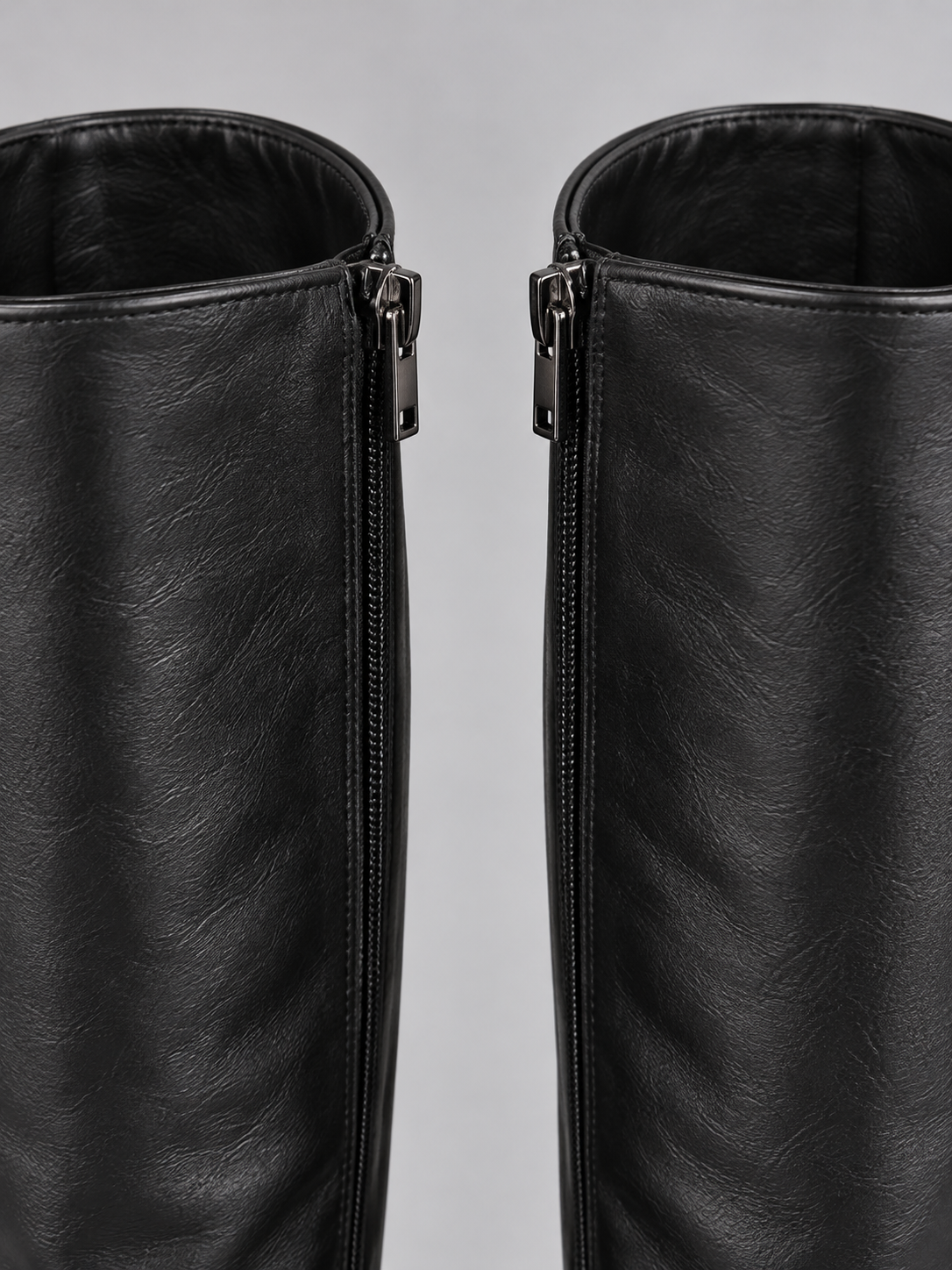 Close-up of the upper shafts of the black knee-high boots, highlighting the side zip closures and softly textured gathered finish.