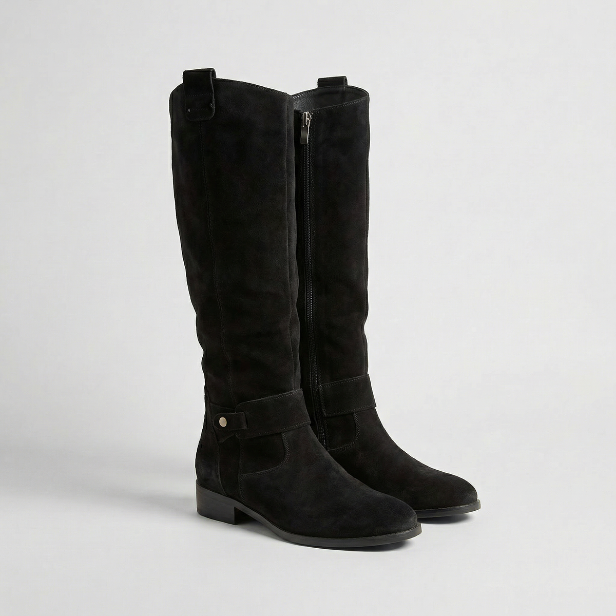 Black knee-high boots featuring gathered shafts, visible side zippers, ankle buckle straps, rounded toes and low heels.