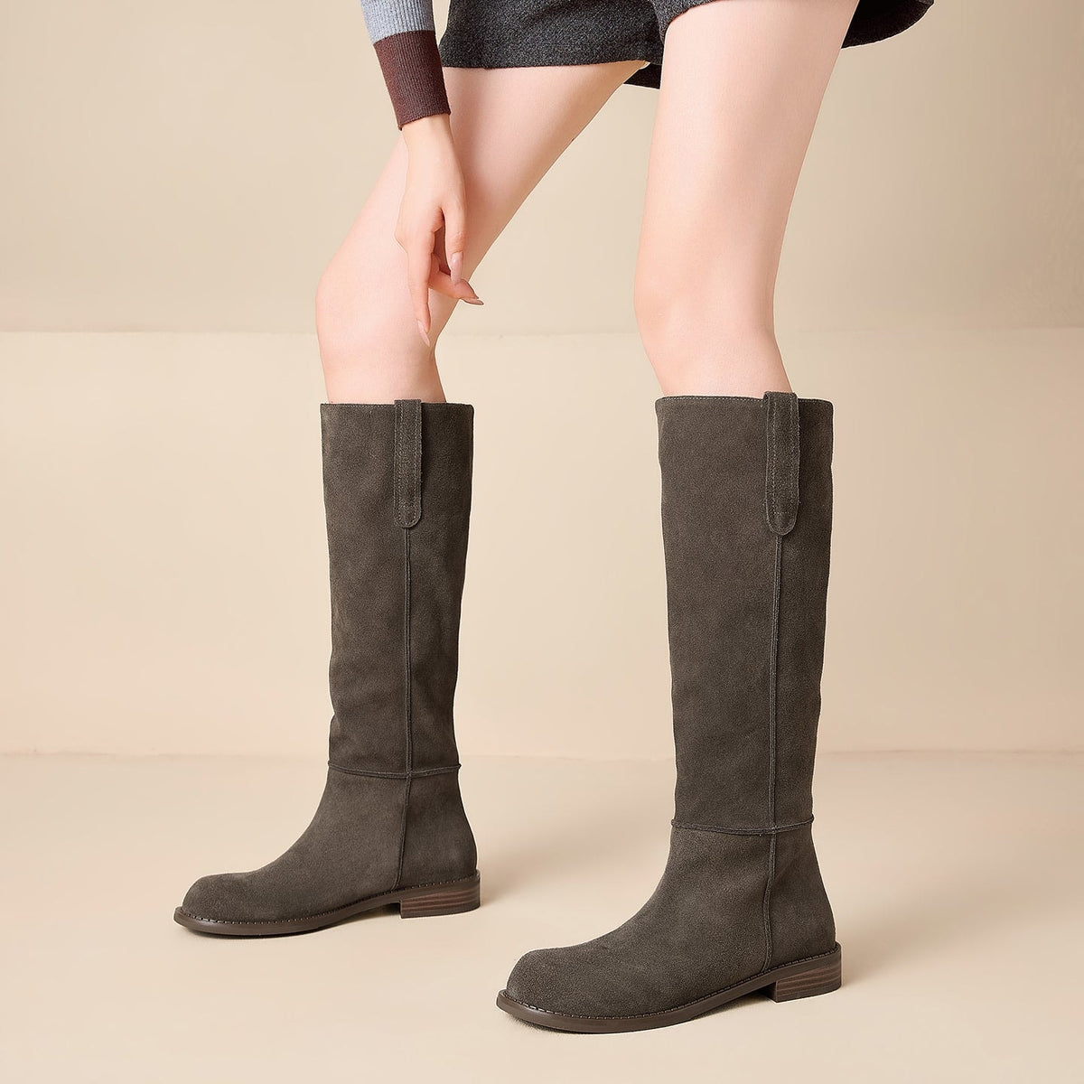 Pair of charcoal gray knee-high boots with rounded toes and low stacked heels worn with a dark skirt.