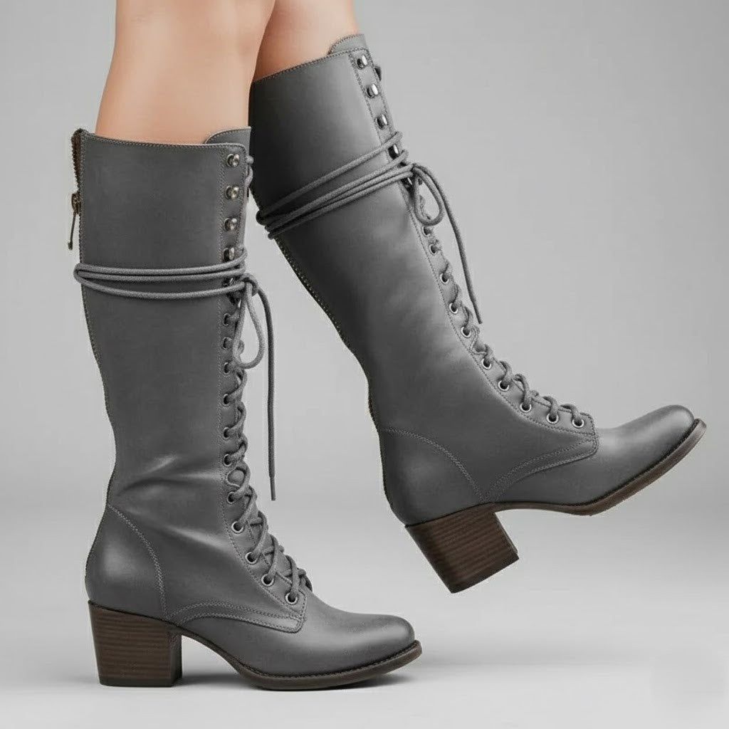 Gray lace-up knee-high boots modeled in motion, showing the side profile, extended shafts, and block heels.