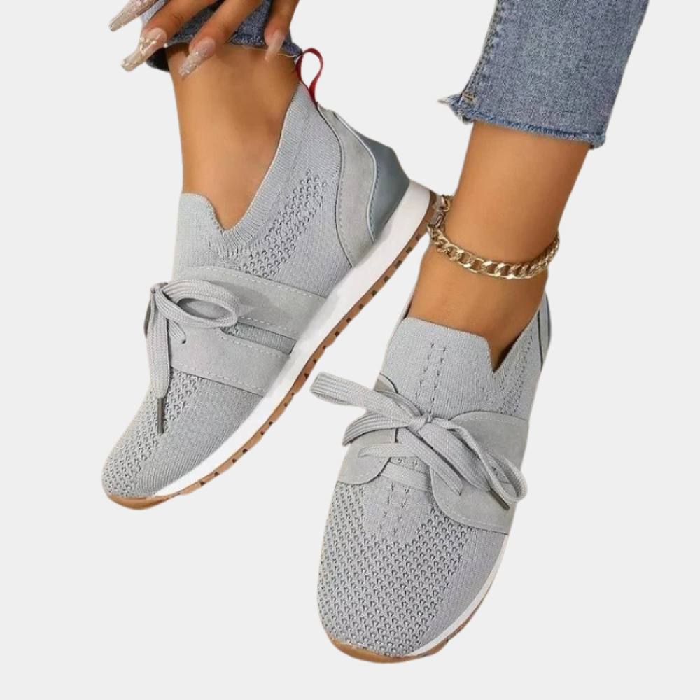 Pair of light gray low-top lace-up everyday sneakers with textured uppers, padded collars, and contrasting white soles with brown-toned outsoles, shown worn with rolled jeans.