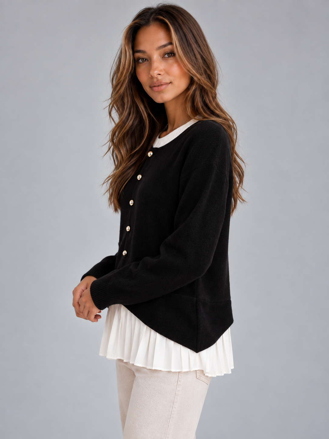 Side view of the black cardigan showing the relaxed fit, buttoned front, curved hem, and pleated white panel extending below it.