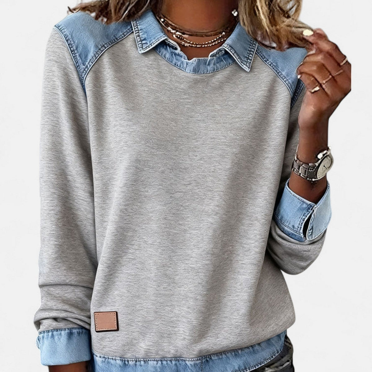 Close front view of the gray sweater with blue layered collar, shoulder accents, and lower hem panel.