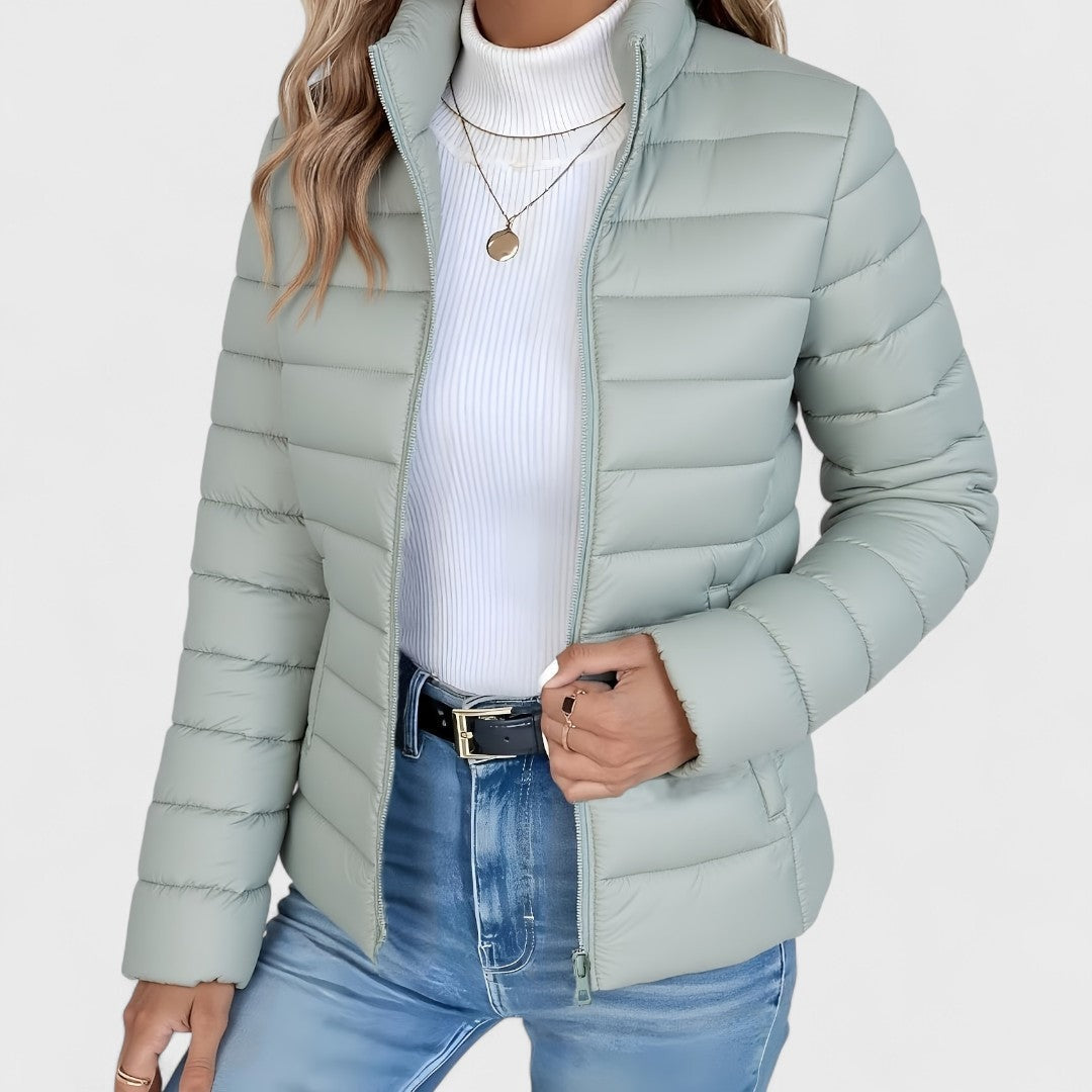 Light sage quilted jacket shown from the front with the stand collar raised and one hand holding the zipper area.