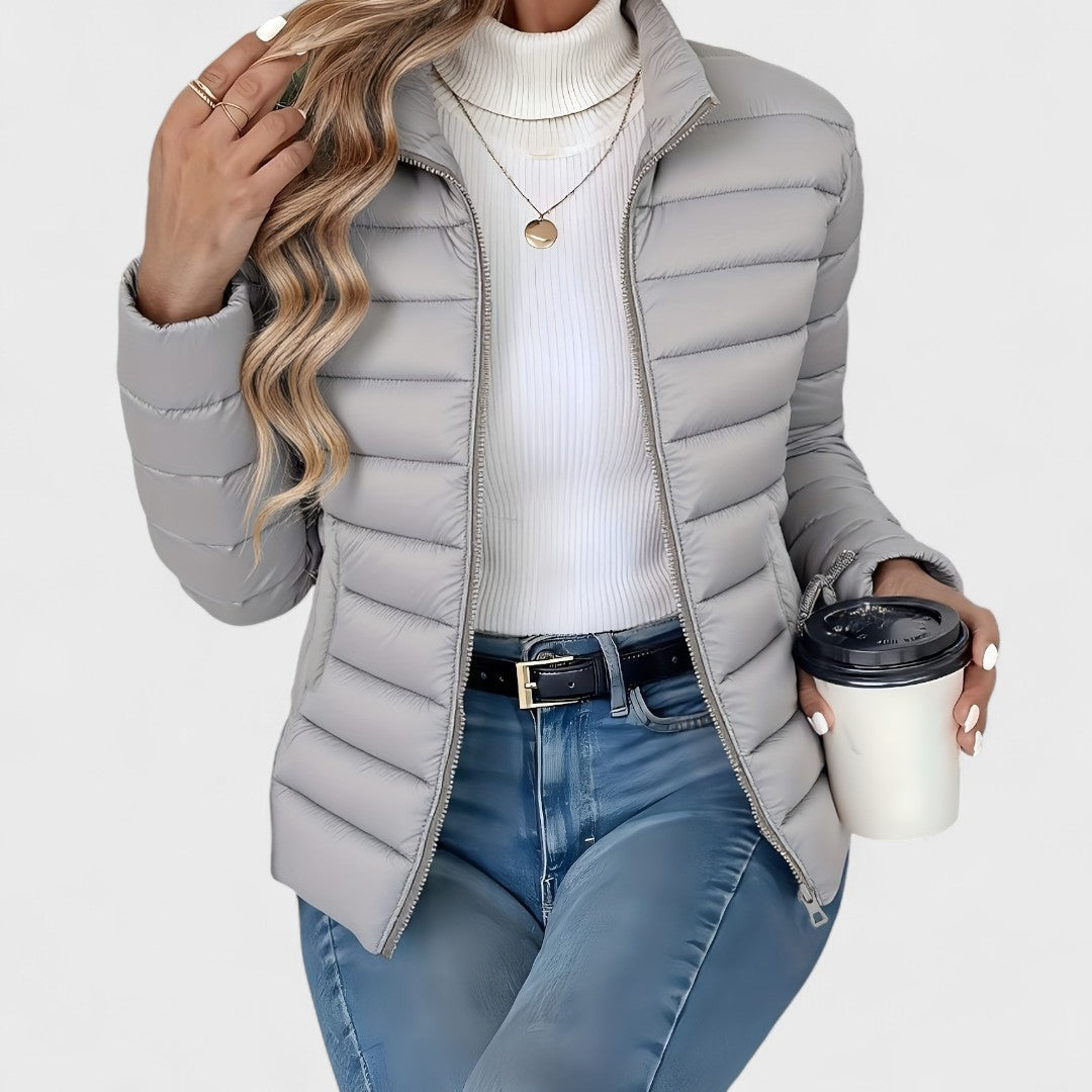 Light gray quilted jacket with an open front, raised stand collar, and long sleeves styled over a white turtleneck.