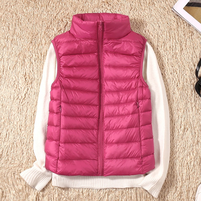 Bright pink quilted zip-up vest arranged over a white sweater, with its fitted sides and front pockets clearly shown.