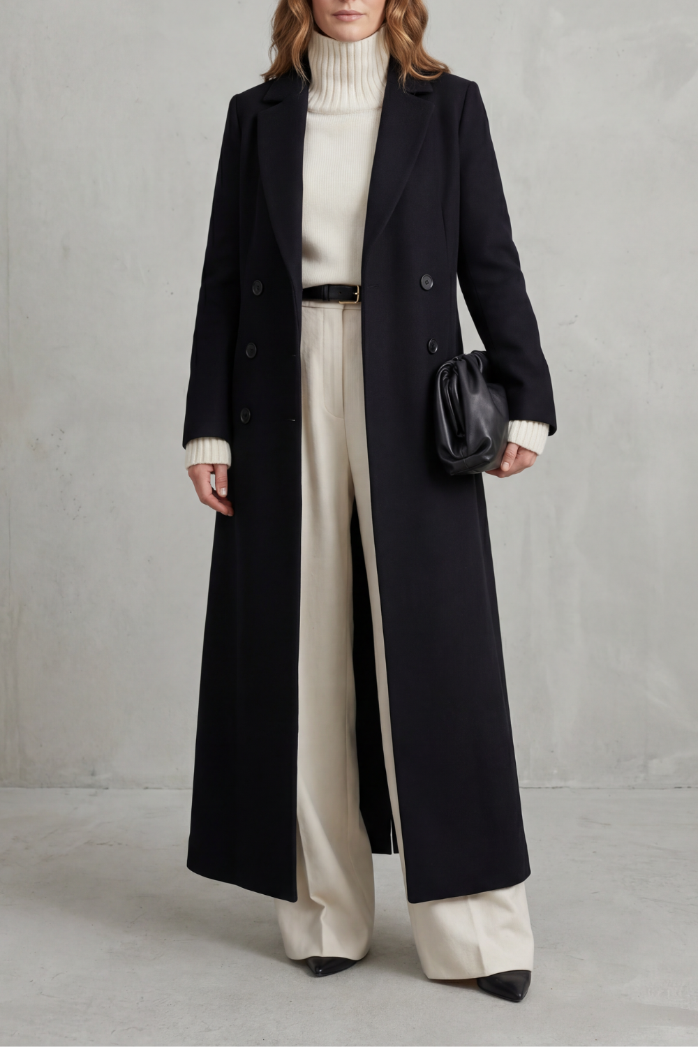 Front view of a black long double-breasted tailored coat with notched lapels, long sleeves, and a straight full-length silhouette.
