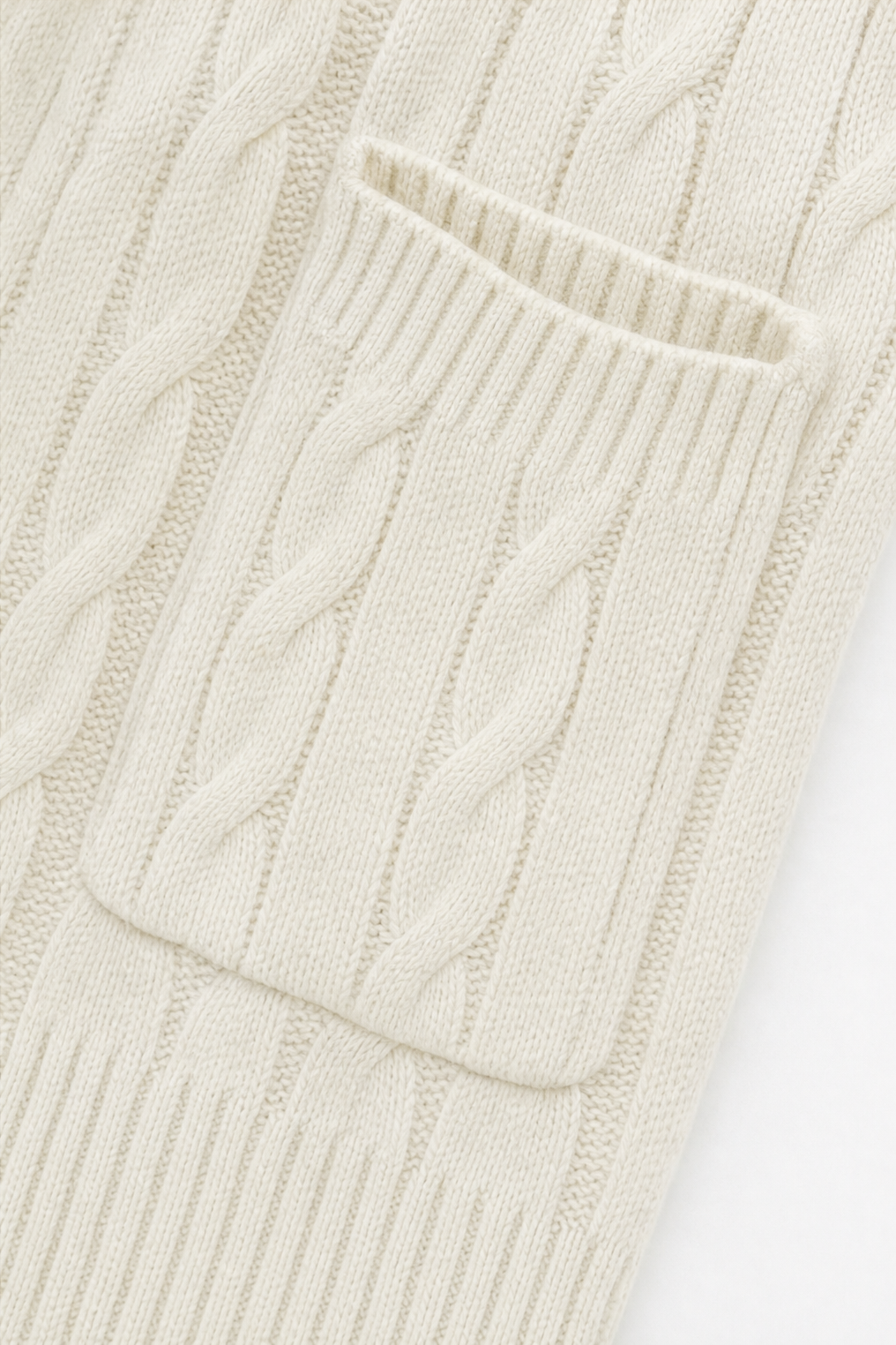 Close-up of one front patch pocket on the cream cardigan, surrounded by the vertical cable knit pattern.