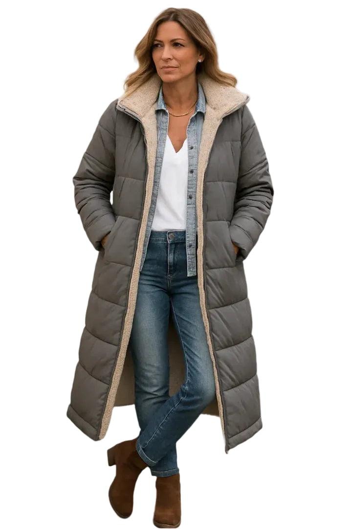 Model wearing a grey long quilted coat with both hands in the side pockets and horizontal quilting visible across the body.