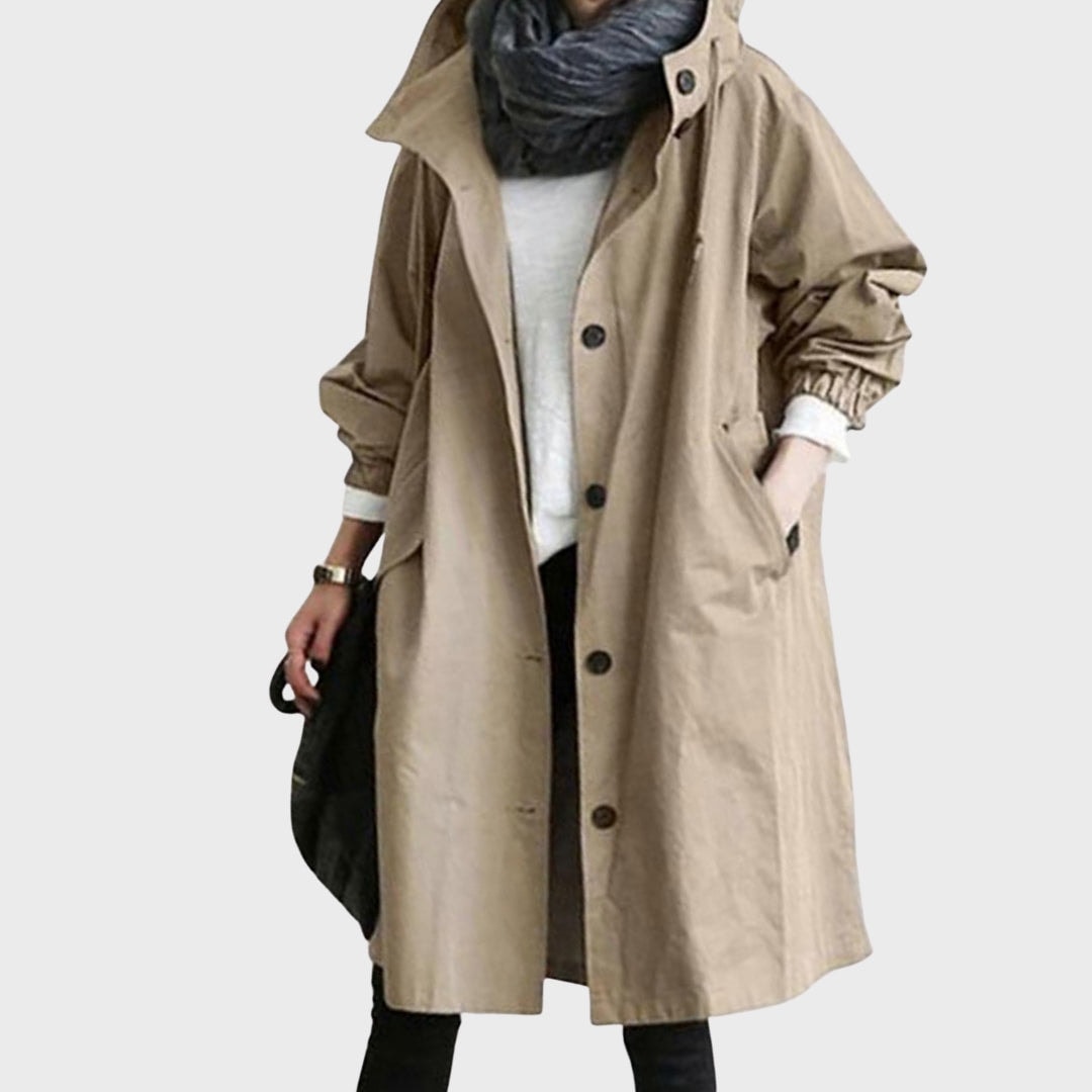 Front view of the rain coat in tan, worn open over a light top with the hood folded behind the neck.