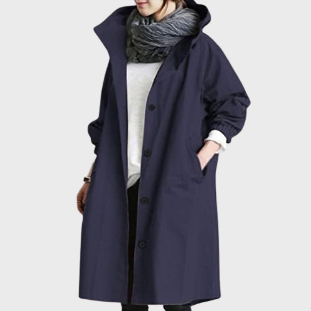 Front view of the rain coat in deep navy, showing the raised hood, button front, and hands tucked into the side pockets.