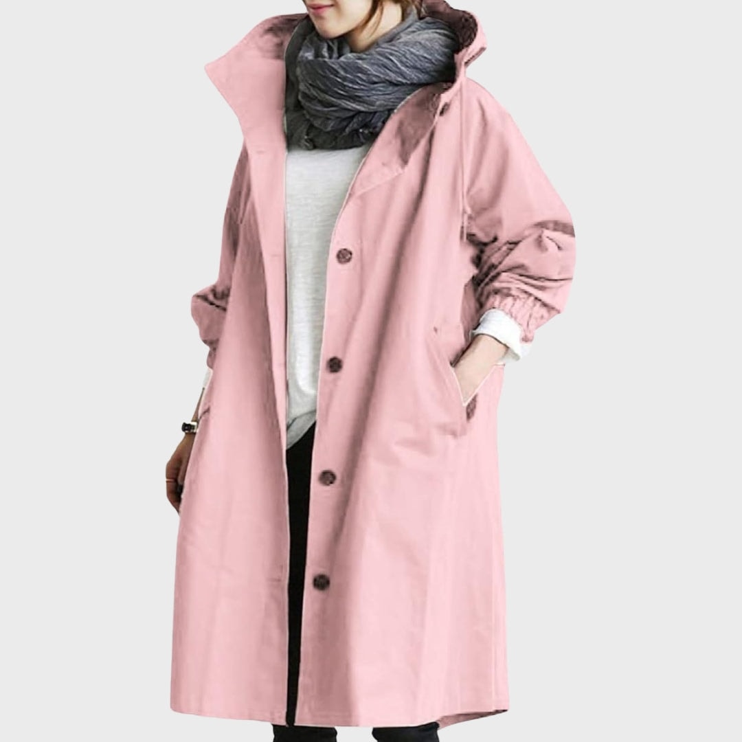 Front view of the rain coat in pink, highlighting its long coverage, raised hood, dark buttons, and elasticated sleeve cuffs.