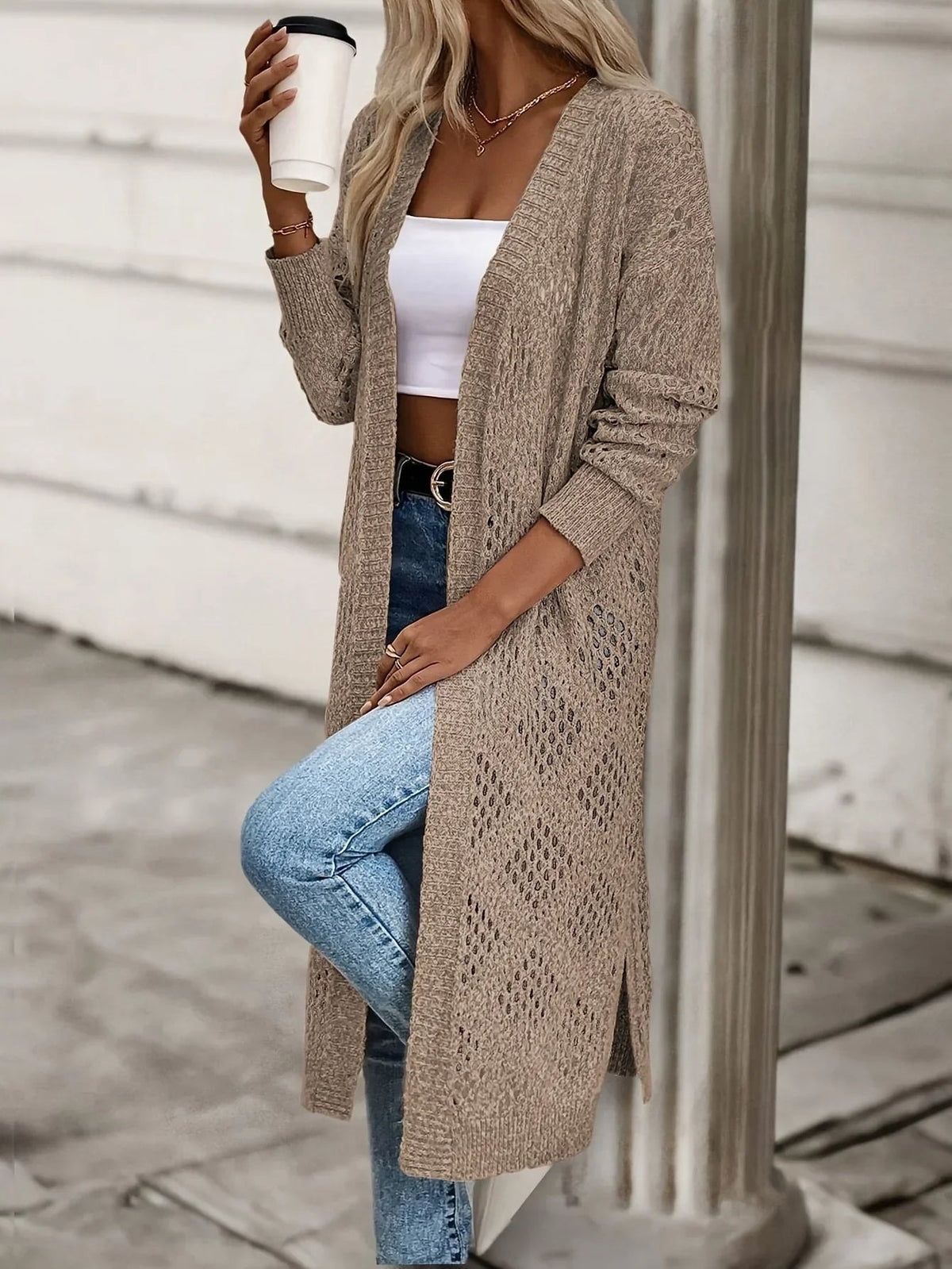 Three-quarter view of the long cardigan highlighting the textured diamond openwork, open front, long sleeve, and side slit while styled with jeans.